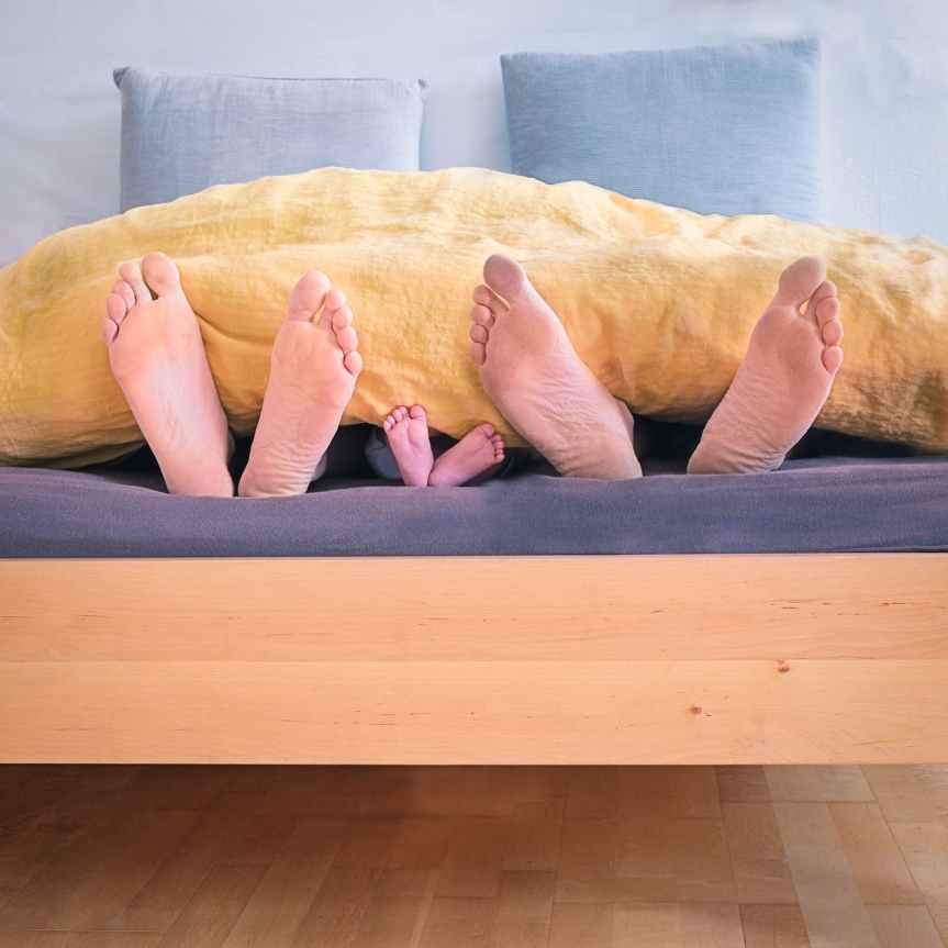 family of three lying on bed showing feet while covered with yellow blanket